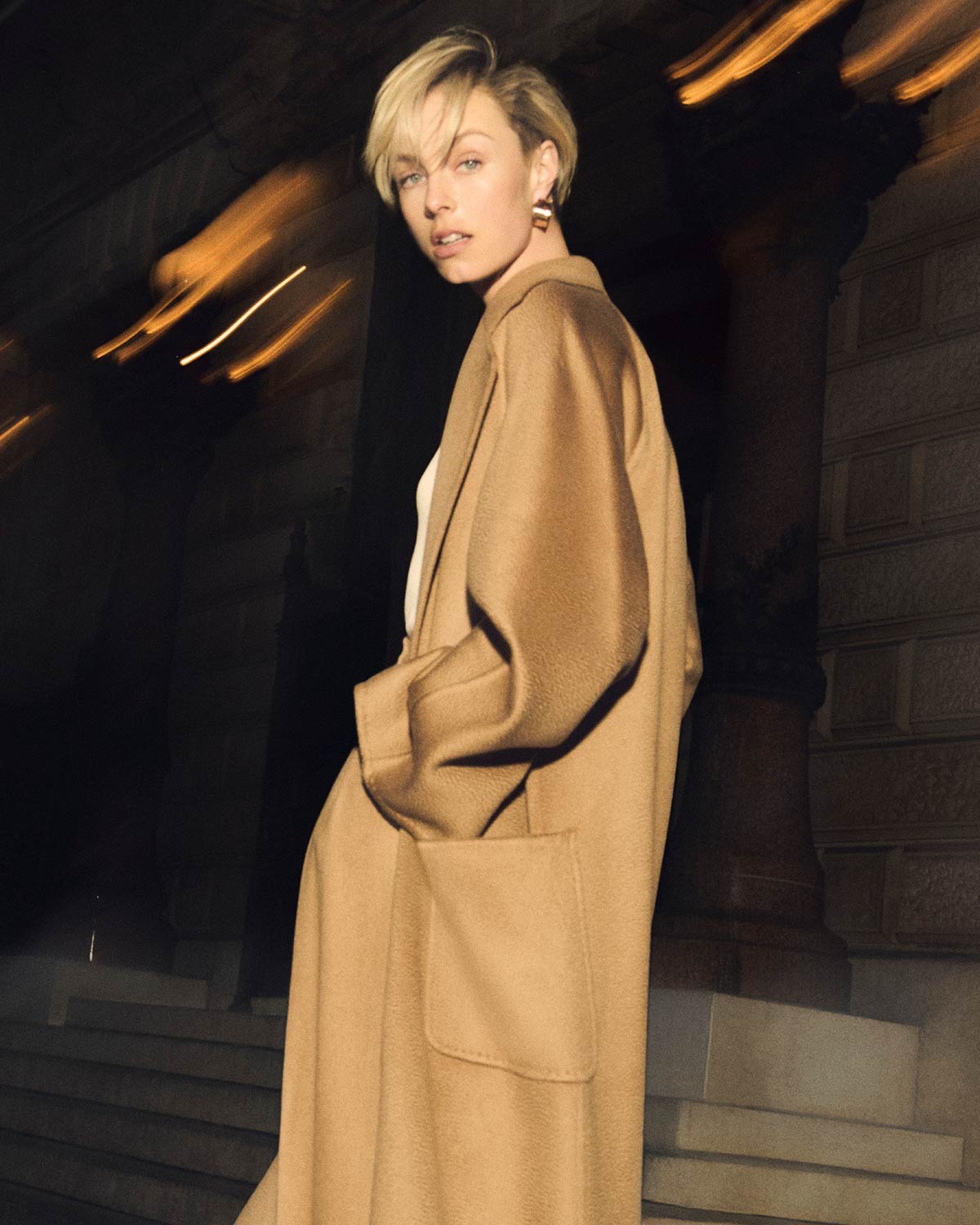 Mannequin portant le manteau iconique large Ludmilla de Max Mara couleur chameau, en soirée.