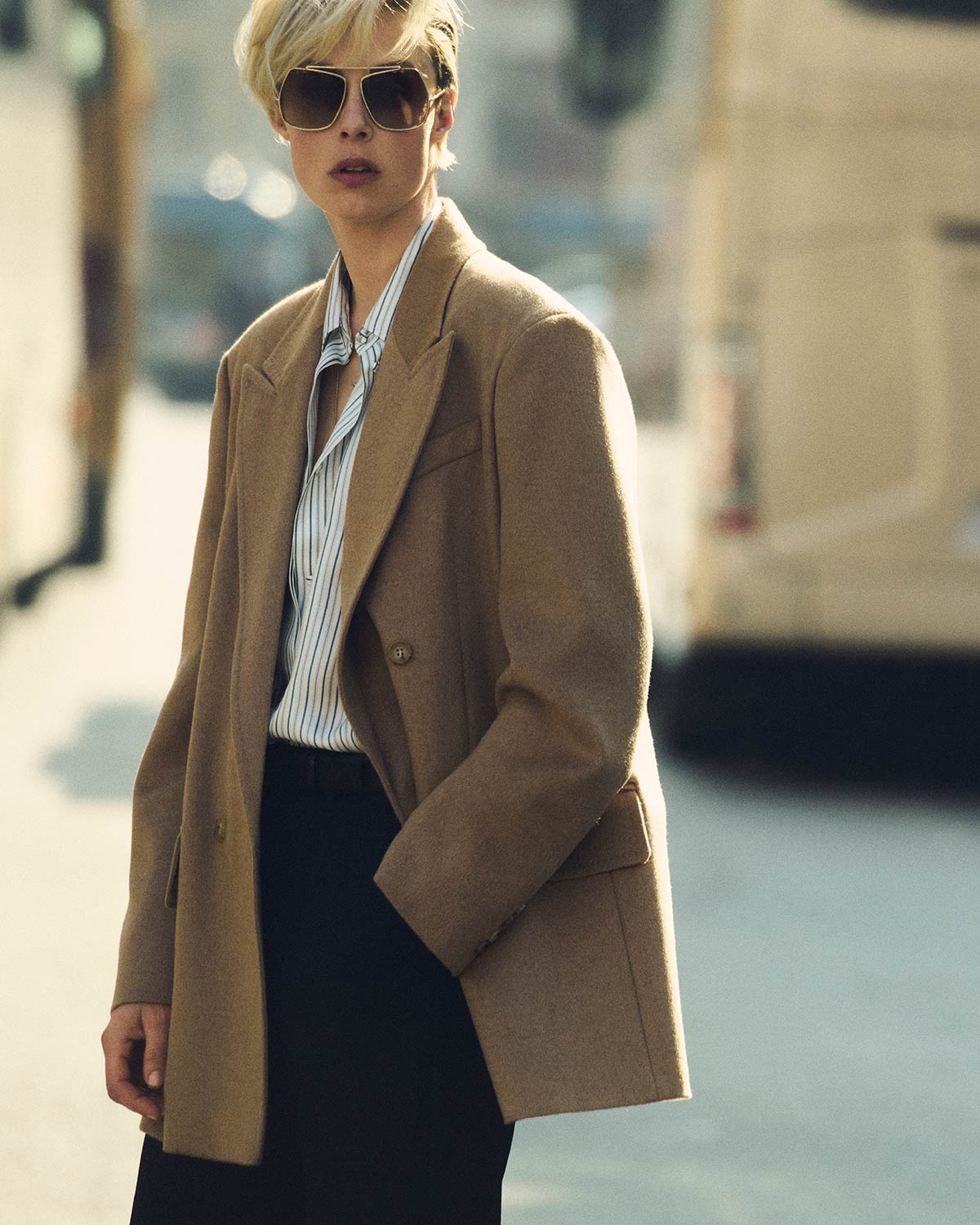 Mannequin portant le blazer double boutonnage Olimpia Jacket de Max Mara couleur chameau avec des lunettes de soleil et une chemise en milieu citadin.