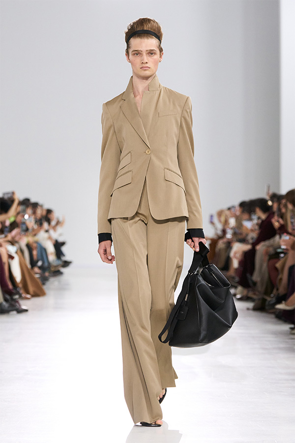 Défilé Max Mara Printemps Été 2026 : look beige avec tailleur et pantalon couleur unie avec sac noir à la main.
